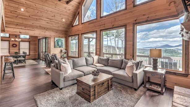 Un salon spacieux avec un grand canapé d’angle, une table basse en bois et une vue sur les montagnes grâce à de grandes fenêtres.