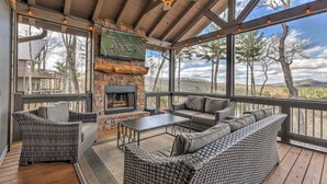 Un espace extérieur aménagé, abrité et doté de mobilier en osier, d’une cheminée en pierre et offrant une vue sur le paysage environnant.