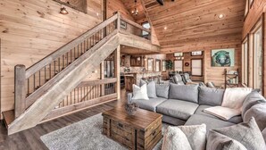 Un vaste espace de vie agrémenté d’un escalier en bois, d’un grand canapé d’angle gris et d’une table basse en bois rustique.