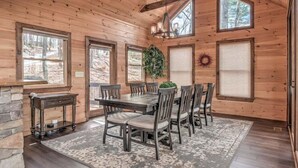 L’intérieur d’un chalet en bois comprend une table à manger, des chaises, une petite table d’appoint et une grande fenêtre donnant sur une forêt.