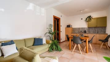 Ein Wohnzimmer mit einer Couch, einem Esstisch mit Stühlen, einer Küchenzeile und einer Tür zu einem anderen Raum.