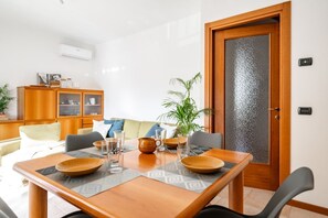 Ein Essbereich mit einem Holztisch, gedeckt für vier Personen, umgeben von Stühlen. Links befindet sich eine Vitrine mit Glastüren und rechts eine Tür mit einer satinierten Glasscheibe.