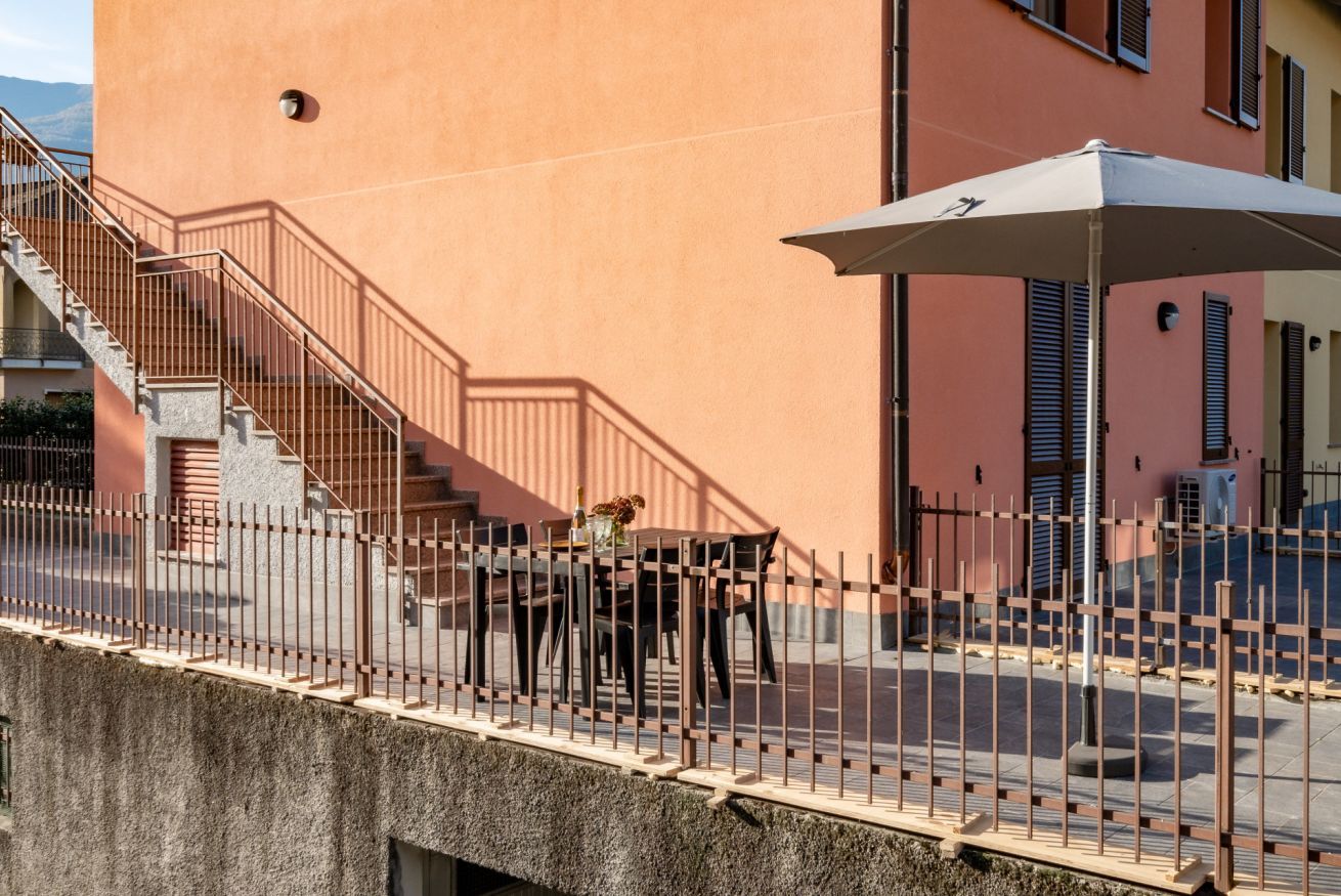 Un bâtiment doté d’un escalier menant à un balcon, d’une clôture et d’un espace extérieur aménagé avec des sièges et un parasol.