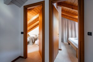 Een kamer met een schuine kap, houten balken, een bed, een nachtkastje en een raam met gordijnen.