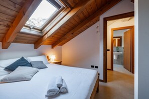 Ein Schlafzimmer mit Oberlicht, einem Bett mit Kissen und Handtüchern, einem Nachttisch mit Lampe und einem durchgehenden Türspalt sichtbaren Badezimmer.
