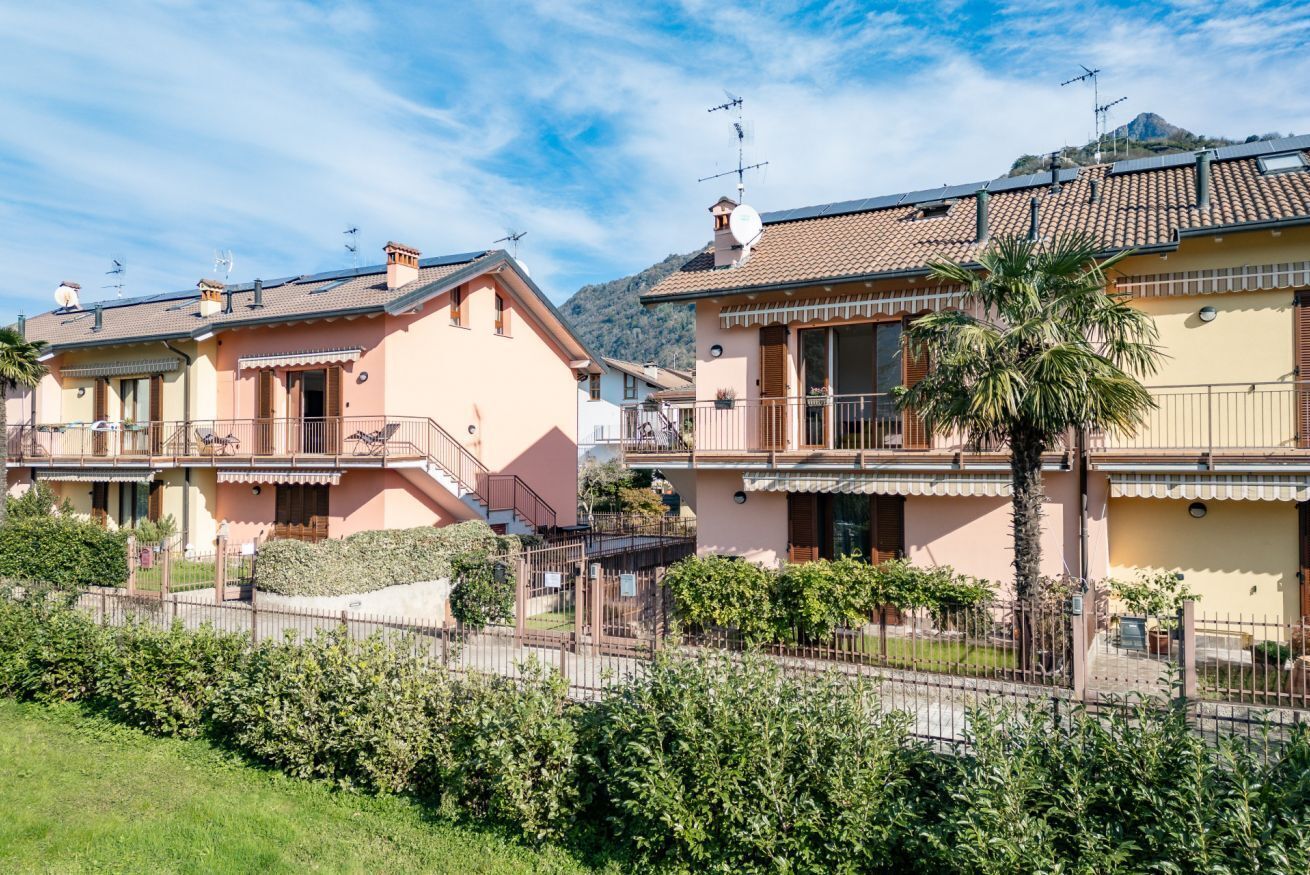 A row of Mediterranean-style houses with balconies, a clear sky, and a mountain in the background.