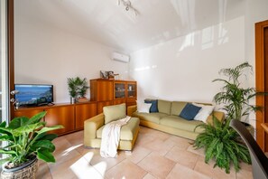 Una sala de estar con sofá, televisor, aparador y plantas en macetas.