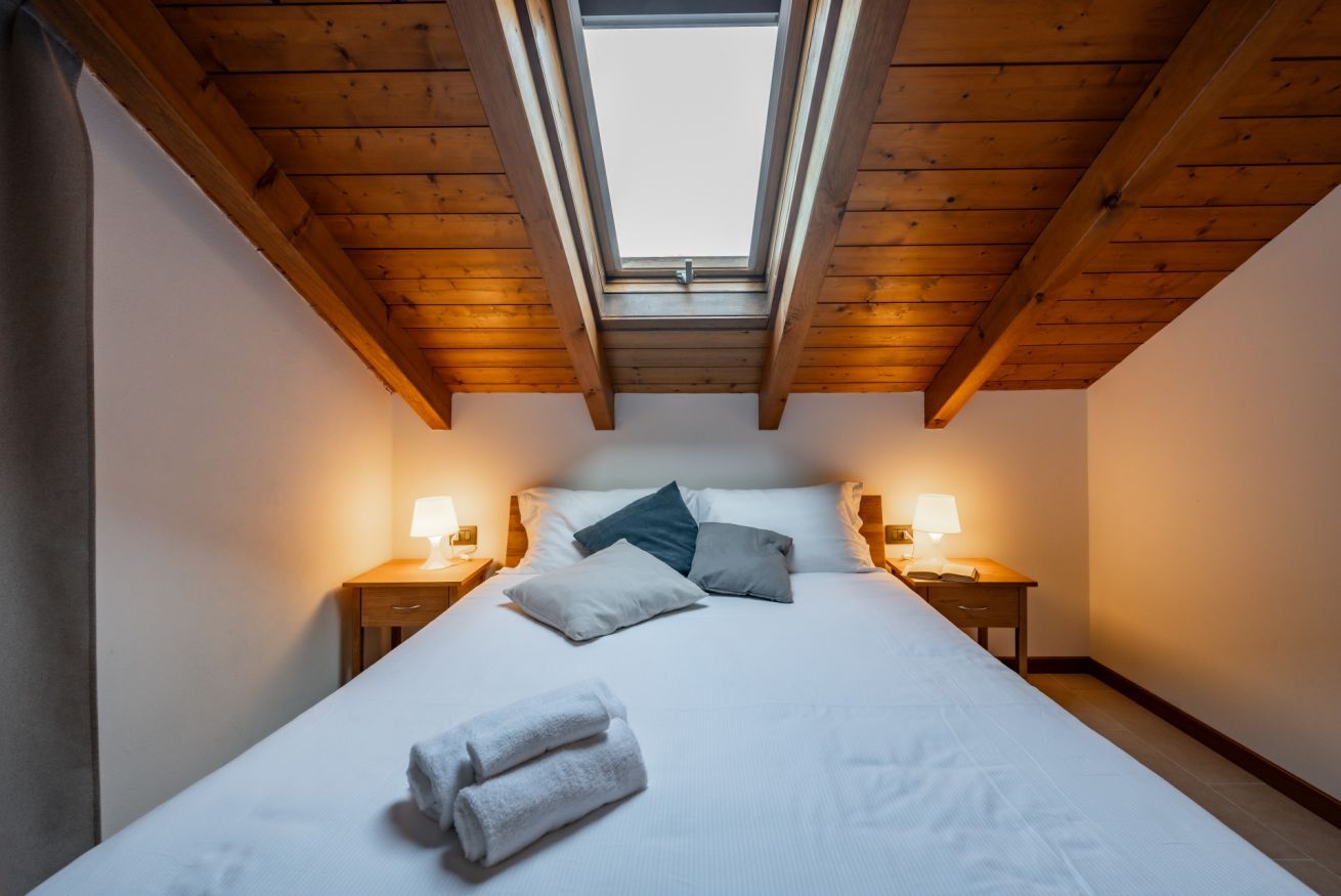 Une chambre avec une lucarne, un lit avec des oreillers, deux tables de chevet avec des lampes et une paire de serviettes sur le lit.