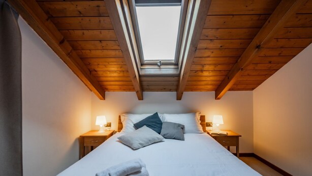 Une chambre avec une lucarne, un lit avec des oreillers, deux tables de chevet avec des lampes et une paire de serviettes sur le lit.
