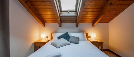 A bedroom with a skylight, a bed with pillows, two bedside tables with lamps, and a pair of towels on the bed.