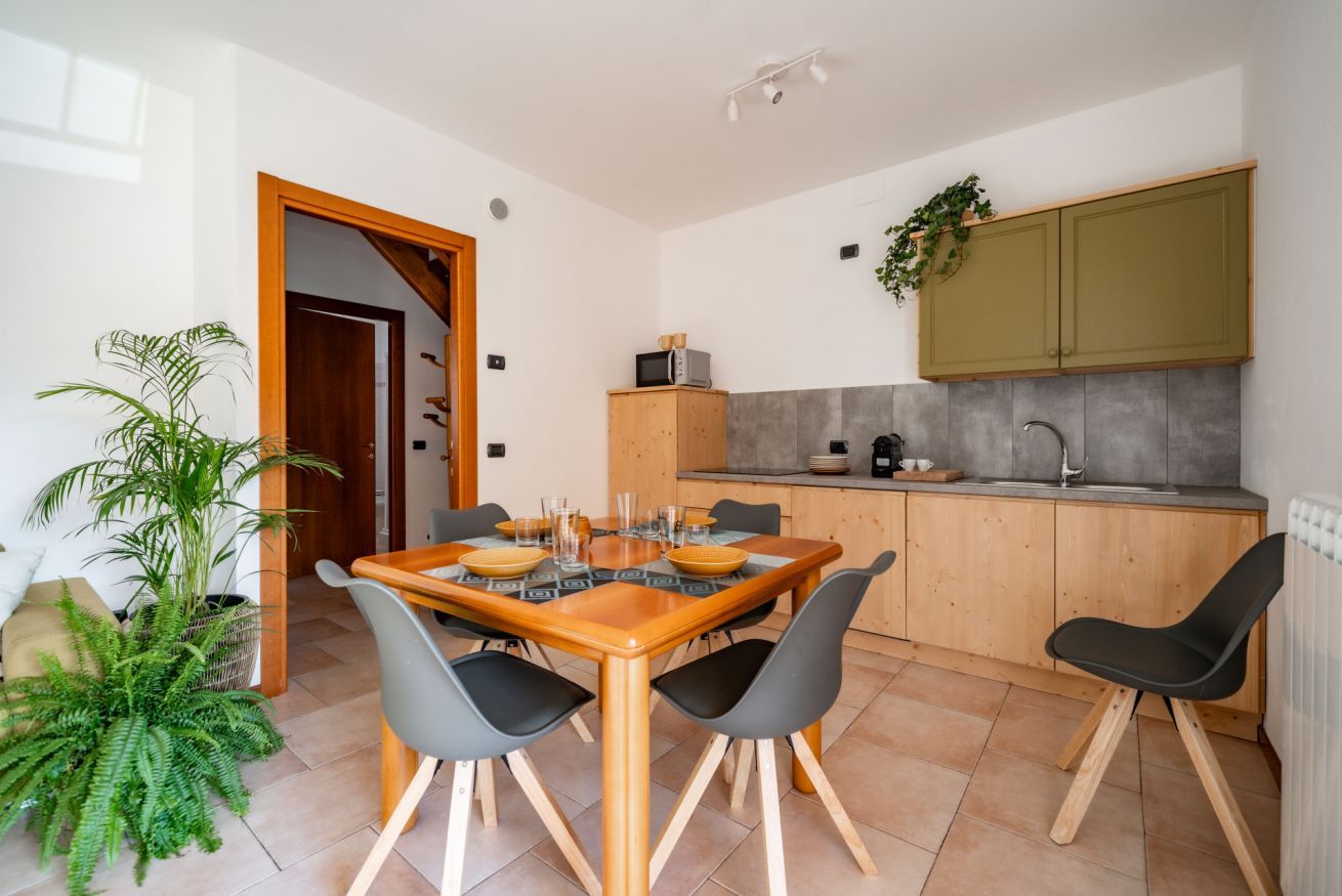 Une cuisine moderne avec des meubles en bois, un four à micro-ondes encastré et un évier. On y trouve une table à manger avec des chaises et une plante en pot.