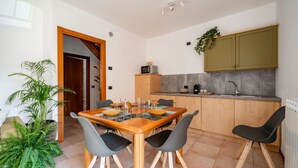Une cuisine moderne avec des meubles en bois, un four à micro-ondes encastré et un évier. On y trouve une table à manger avec des chaises et une plante en pot.