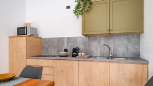 Une cuisine compacte avec des meubles en bois, un crédence carrelé de couleur grise, un évier et un four à micro-ondes posés sur un plan de travail en bois.