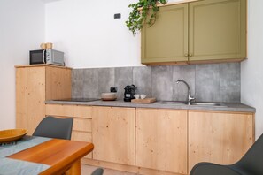 Eine kompakte Küche mit Holzschränken, einer grauen Fliesenrückwand, einer Spüle und einer Mikrowelle auf einer Holzausziehtafel.