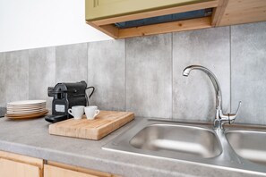 Una cocina con un lavamanos doble, una cafetera y una tabla de cortar con tazas y platos.