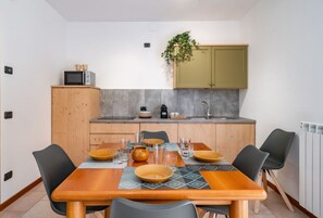 Een compacte keuken met een houten eettafel, een magnetron en een kastje met een plant.