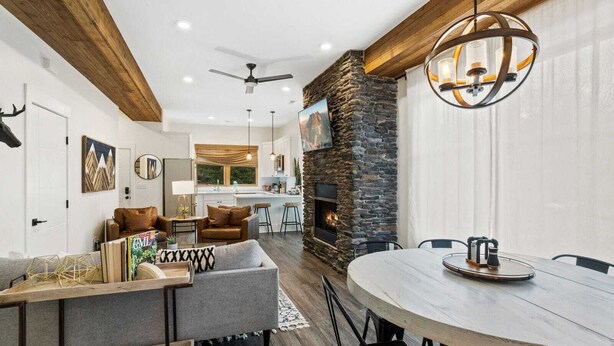 Una sala de estar moderna con chimenea de piedra, un comedor con mesa redonda y una cocina al fondo.