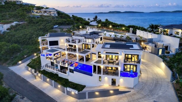 Una casa moderna de varios pisos con piscina, varios balcones y vista al mar.