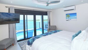 Un dormitorio con una cama grande, vista al océano, ventilador de techo y aire acondicionado.