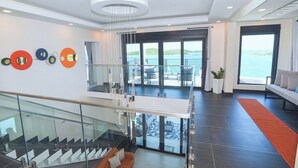 Un interior moderno con una escalera de vidrio, una zona de estar con sofá y vistas al mar.