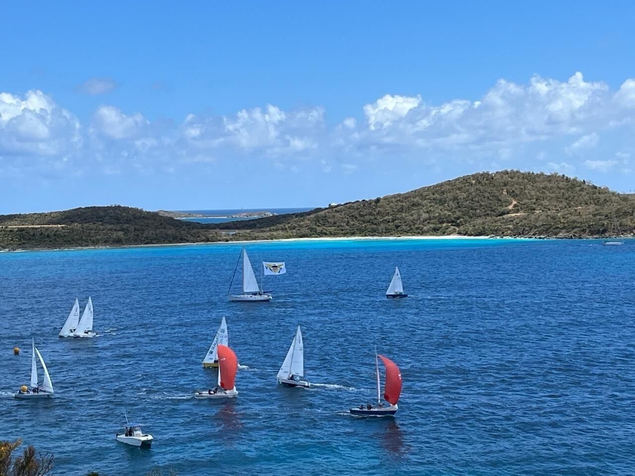 A coastal scene with sailboats on the water, a clear sky, and a hilly landscape in the background.