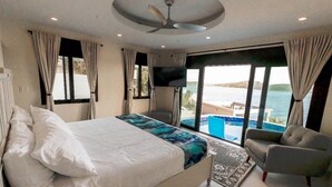 Un dormitorio con cama, televisor, una silla y vista al mar.