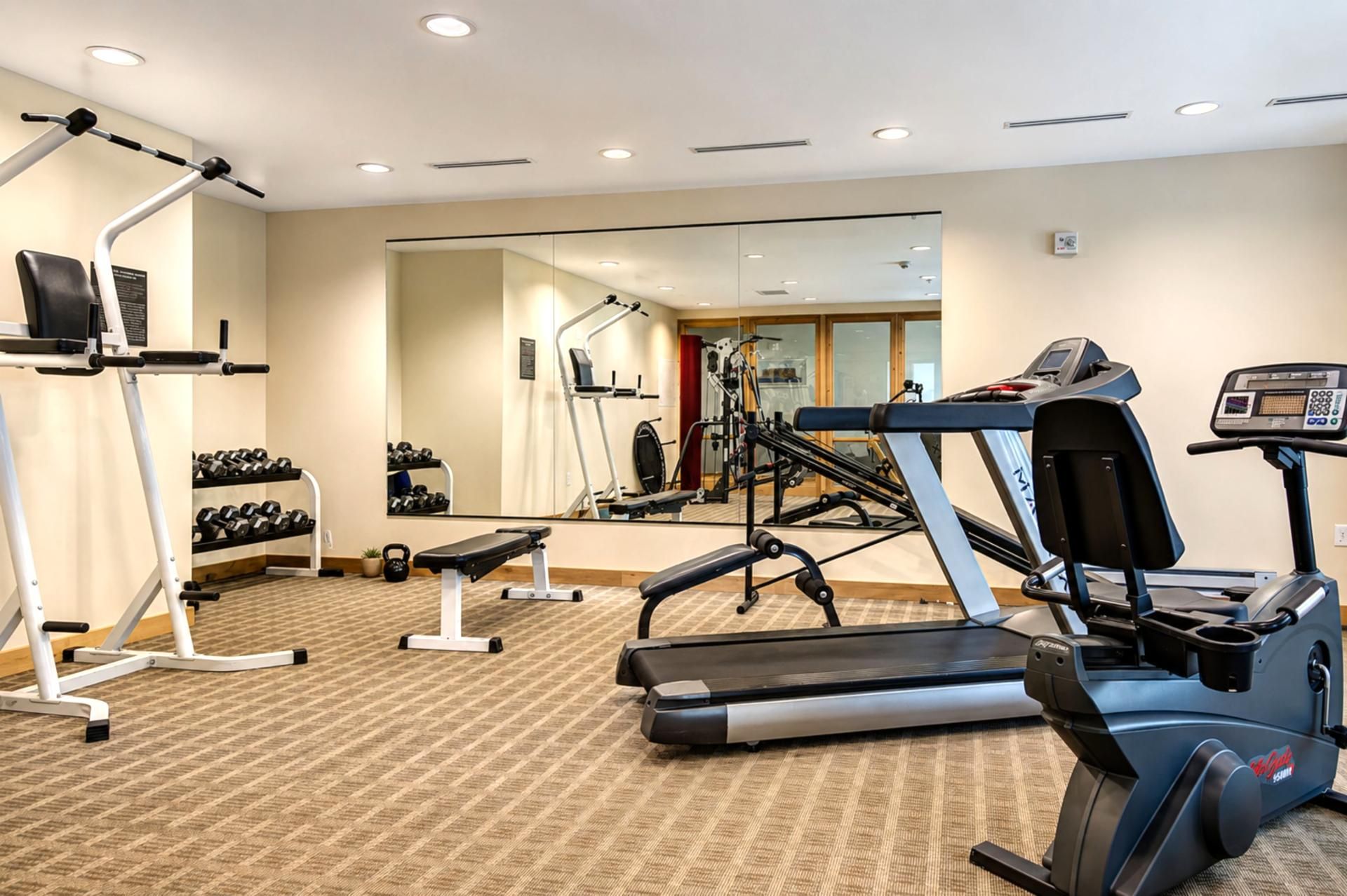 Ett gym med träningsutrustning, inklusive löpband, en bänk och hantlar.