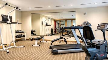 Ett gym med träningsutrustning, inklusive löpband, en bänk och hantlar.