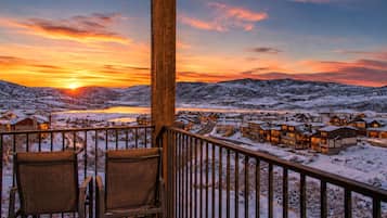 Une terrasse en bois avec deux chaises, d’où l’on peut admirer un village enneigé, avec des bâtiments et des montagnes en arrière-plan.
