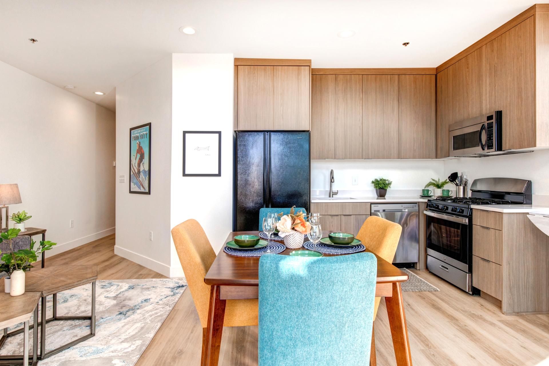 A modern kitchen with wooden cabinets, a black refrigerator, a stove, and a microwave. There is a dining table with chairs and a rug on the floor.