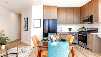 A modern kitchen with wooden cabinets, a black refrigerator, a stove, and a microwave. There is a dining table with chairs and a rug on the floor.