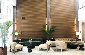 A lobby with a high ceiling, wooden panel walls, and a seating area with sofas and armchairs.