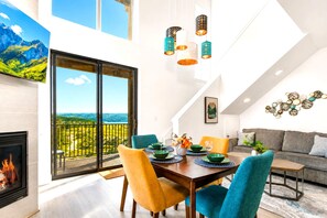A dining area with a view of a mountainous landscape through large windows, a fireplace, and a modern chandelier.