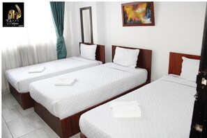 Une chambre d’hôtel avec trois lits simples, du linge de lit blanc, un grand miroir et un tableau coloré accroché au mur.