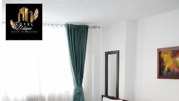 Habitación de hotel con dos camas individuales, un ventanal con cortinas translúcidas, un espejo y un cuadro en la pared.