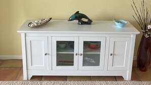 Un mobile bianco con ante in vetro, una TV a schermo piatto montata sulla parete sopra e un vaso con rami sulla destra.