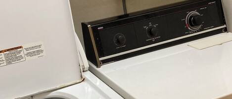 A front-loading washing machine with a control panel, a detergent bottle, and a folded towel on a shelf.