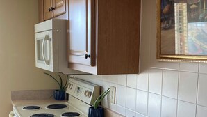 Cucina con mobili in legno, piano cottura bianco, forno a microonde e lavello con dispenser per sapone.