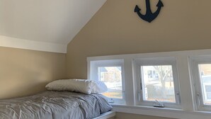 Une chambre à coucher avec un lit, un ventilateur de plafond, une fenêtre et un élément de décoration représentant une ancre.