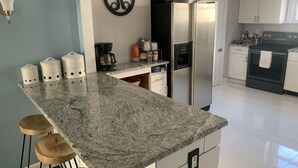 Une cuisine dotée d’un plan de travail en granit, de meubles blancs, d’un réfrigérateur en acier inoxydable et d’une machine à café.