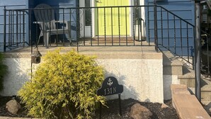 Une maison avec une porte verte, une plaque portant le numéro 131 et un petit porche avec des chaises.