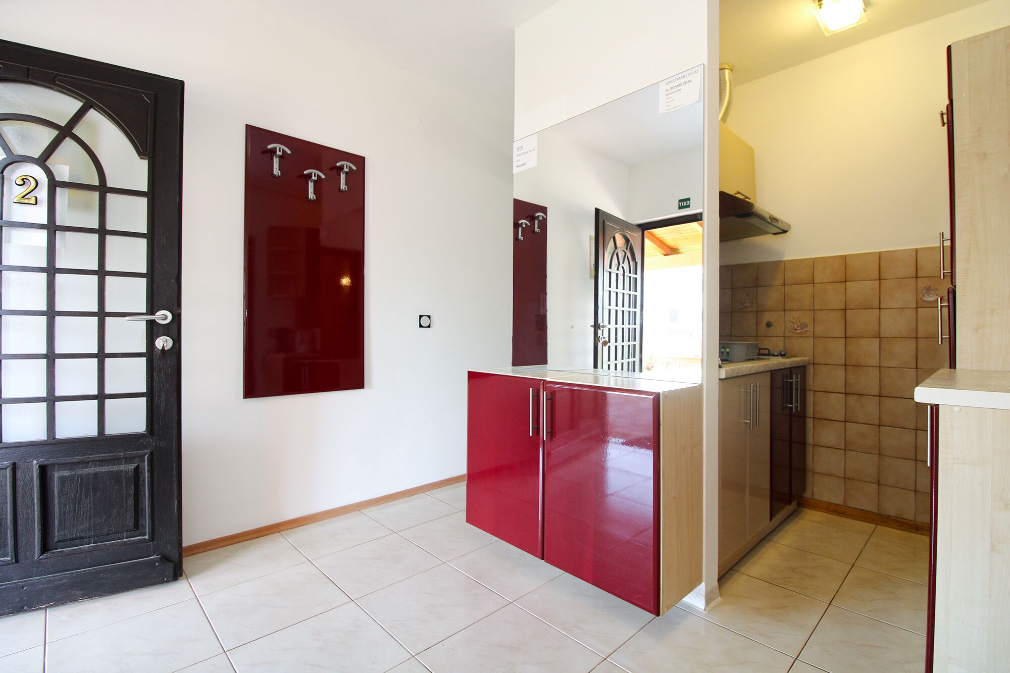 A compact kitchen with a red cabinet, a black door with a glass panel, and a tiled backsplash.