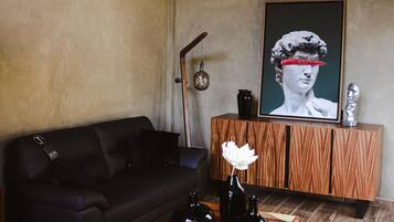 Una sala de estar moderna con un sofá de cuero oscuro, una mesa de centro de madera con jarrones negros y una flor blanca, y una obra de arte enmarcada de gran tamaño en la pared.