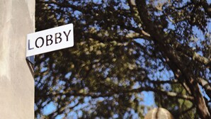 Una señal de calle con la leyenda 'LOBBY', un árbol y un edificio al fondo.