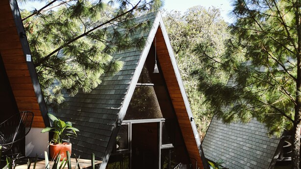 Una casa moderna con techo triangular, rodeada por un jardín con diversas plantas y una terraza de madera.