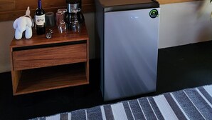 Una habitación con pared de madera, un televisor de pantalla plana sobre una mesita de noche de madera, un refrigerador pequeño y una alfombra a rayas en el suelo.