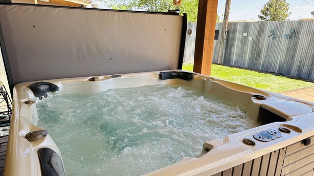 A hot tub with a wooden deck and a metal fence in the background. - Cozy pet friendly house with a great outdoor space, and fully stocked kitchen.   (Las Cruces)