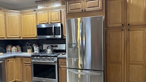 A modern kitchen with wooden cabinets, stainless steel appliances including a refrigerator, stove, and microwave, and a tiled backsplash. - Cozy pet friendly house with a great outdoor space, and fully stocked kitchen.   (Las Cruces)