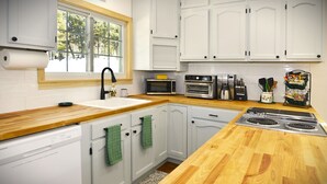 Een keuken met witte kasten, een houten aanrecht, een spoelbak, een magnetron, een broodrooster en een fornuis.