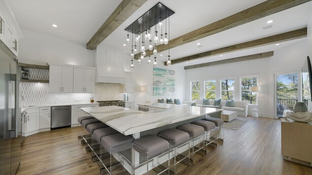 A spacious kitchen with a large island, wooden beams, and a hanging light fixture.